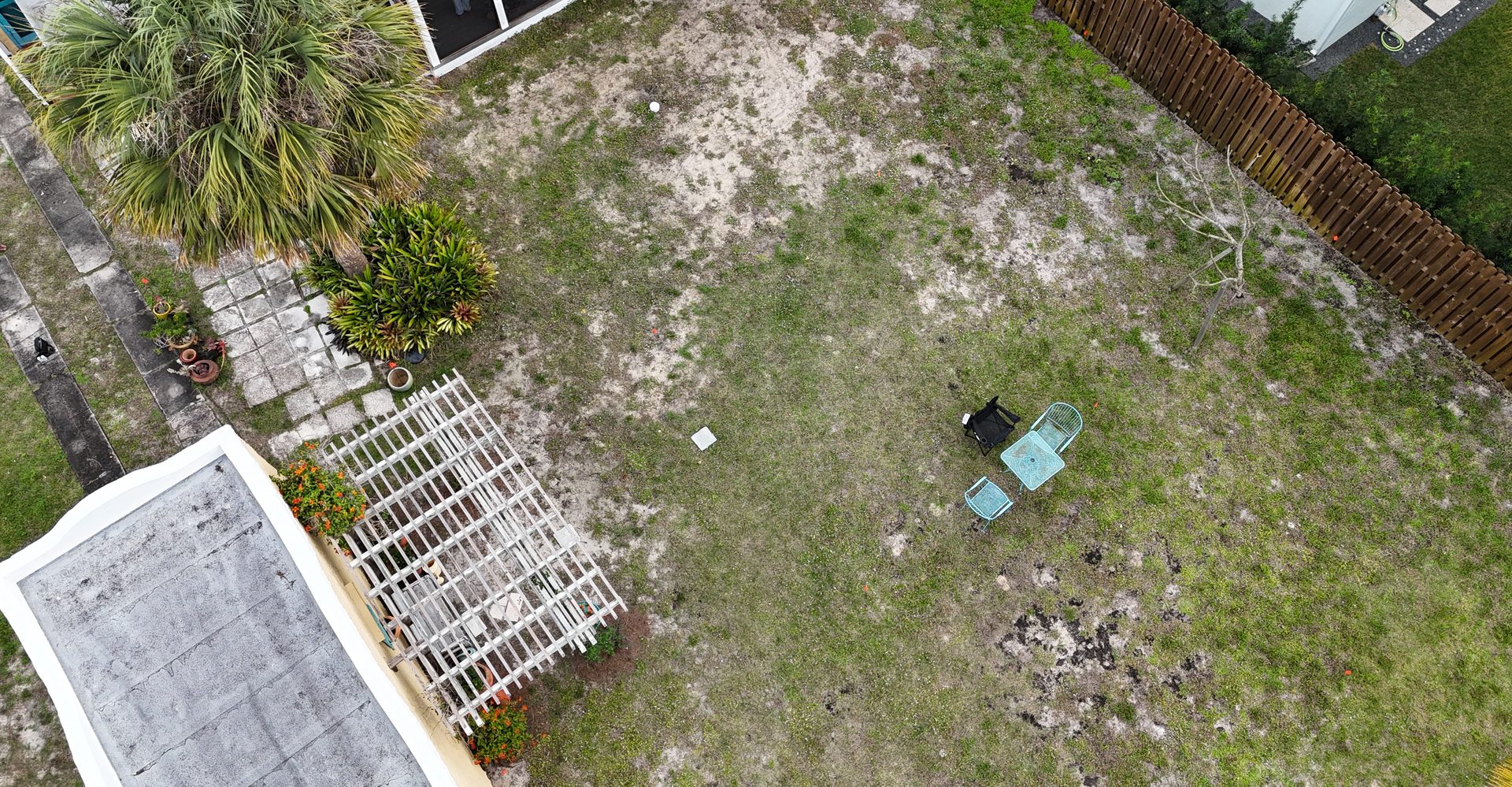 Aerial drone view of a Hobe Sound backyard before installation: bare sugar sand and weeds with a few old sabal palms