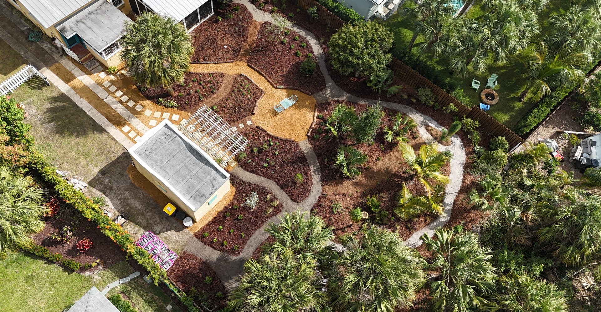 Aerial view of the same Hobe Sound yard just after installation by Longleaf Design: freshly planted native beds in mulched islands with raked sugar-sand nature paths winding between them
